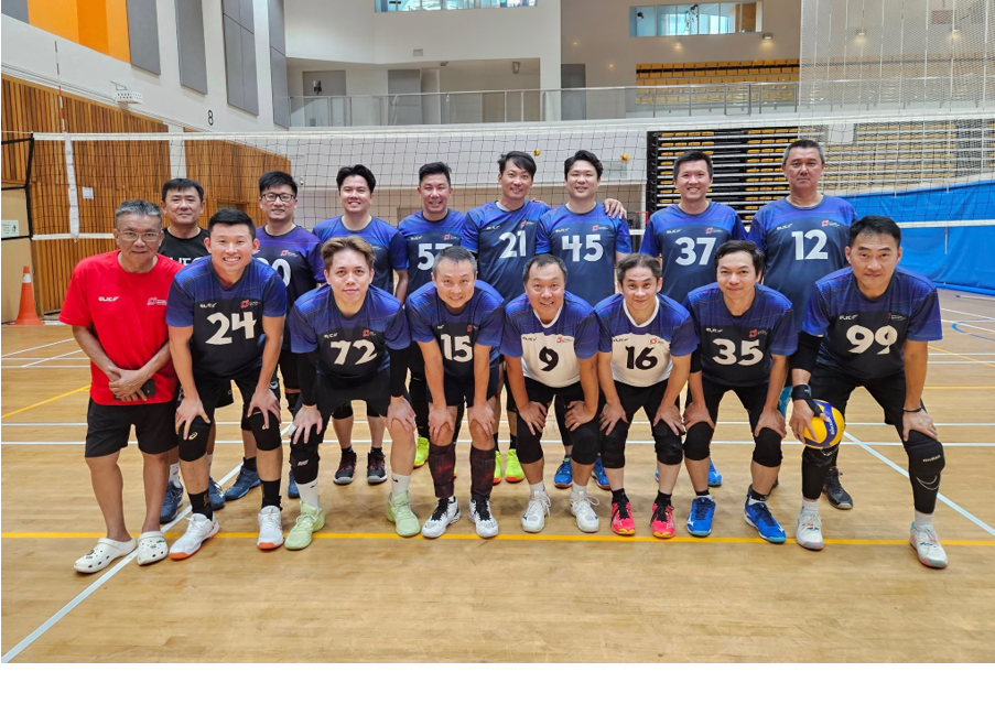 Team of volleyball players in blue uniform posing in front of a net in an indoor court.